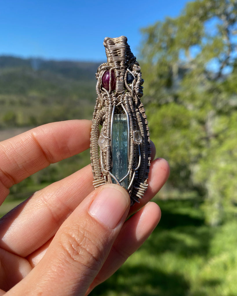 woman holding a wire wrapped crytal necklace with blue and burgundy stones