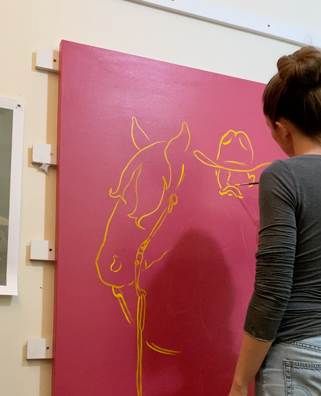 artist Gina Teichert painting a yellow cowboy on a pink canvas